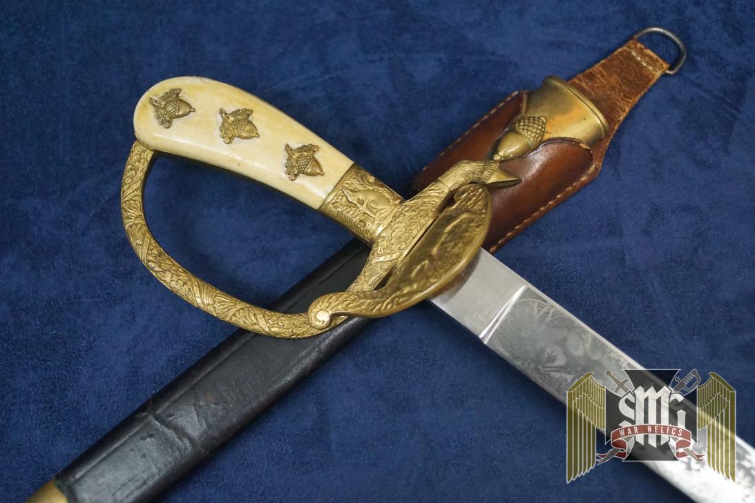 This is a fully loaded model 1059 in the Eickhorn catalogue. The triple etched blade has only the smallest signs of wear and oxidation and easily grades a 9 out of ten and is near mint in all respects. The motifs show a boar getting attacked by hunting dogs with a hunter in pursuit and a hummingbird on one side. The other side is a hunter shooting at deer and a pheasant.  The Eickhorn logo is the early double oval version which makes this blade all the more appealing in my book. The hilt and clamshell still have most of the original gilding and is a real pleasure to examine! My favorite part on these is the Eickhorn squirrel on the front! The clam shell is awesome and depicts a standing stag. The natural ivory grip plates have taken on a yellow tone, as they are un cleaned. The 6 grip acorns are all matching which is nice, since many go missing and are miss matched when replaced. The top one on each side spin a bit but this is ok as they are literally just a tack nail with an acorn head. The dagger is completed by a good condition scabbard with a crease on one side of the leather. The upper and lower fittings are matching numbers (20) and are in great shape. The original frog looks great as well and is complete with the D ring which is often broken off. The back of the frog is finished with green felt to protect the wearer's uniform. A stunning and impressive piece in hand that is sure to be a focal point of your collection! 