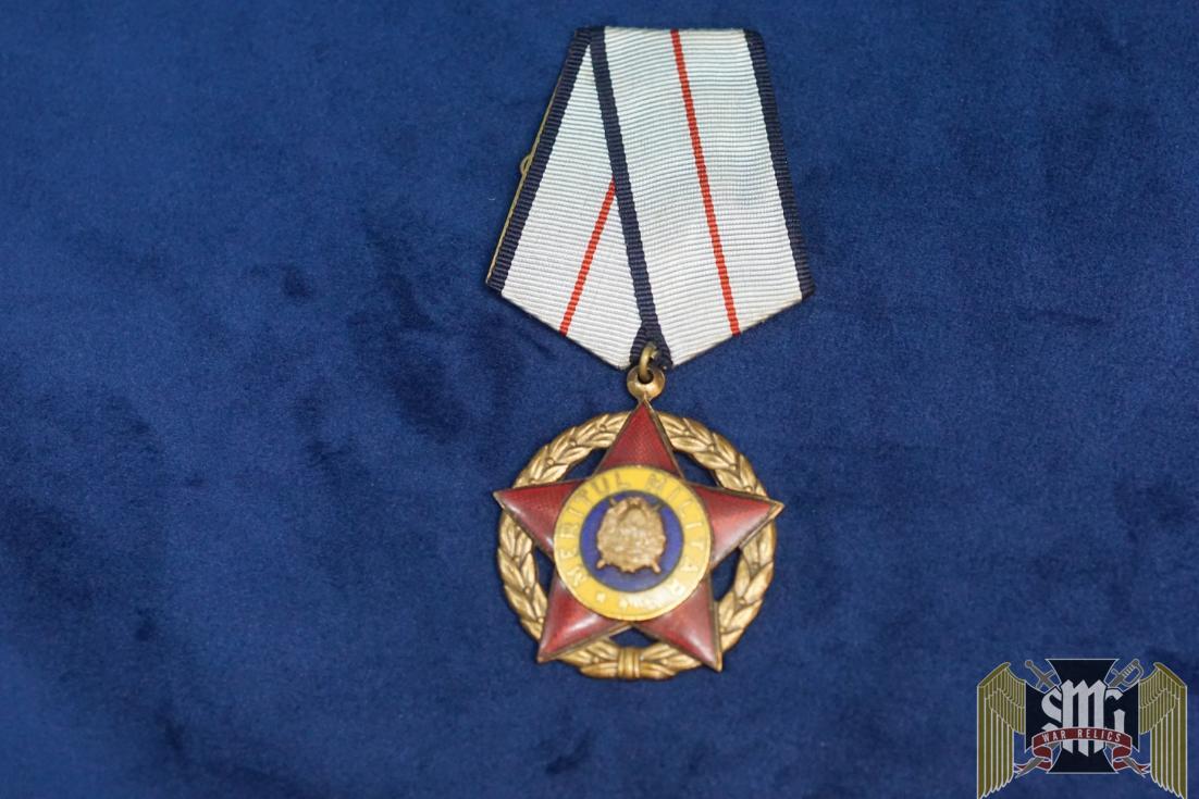 I Class, Gold wreath, Red enamel Star, words in Gold on Yellow background disc, Gold center motif, II Class, Silver wreath, Red enamel Star, words in Silver on Yellow background, Silver center motif, III Class, Bronze wreath, Red enamel Star, words in bronze on yellow background, Silver center motif.